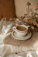 Hot mug of cappuccino on wooden tray on the bed, breakfast, bouquet of dried flowers. Spring scenery. Cozy house. Beige natural colors.