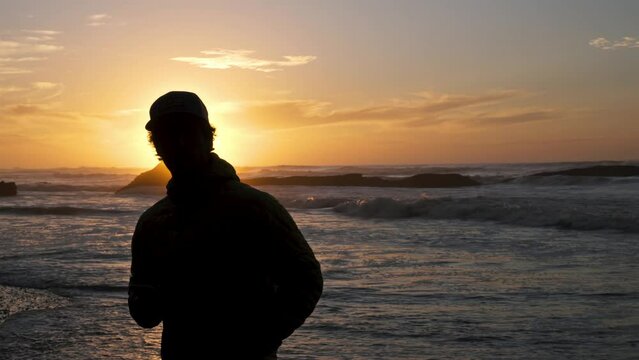Silhouette of young man takes pictures of sunrise on smart phone in Morocco ocean coast beach