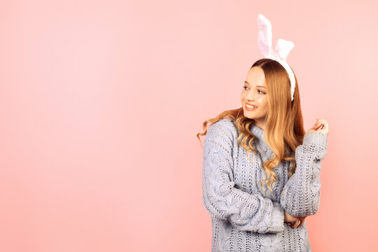 Beautiful girl in a blue sweater on a pink background. Woman with bunny ears, posing for easter, girl smiling, space for text.
