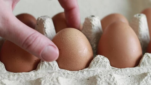 A woman's hand takes an egg from a cardboard box. Fresh raw eggs in a paper egg container. Opening the egg pack, close up. Fresh Protein Food