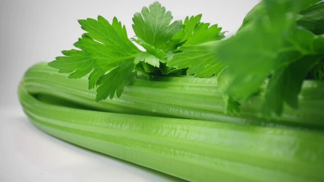 Macro shot fresh green celery stalks lying on white board isolated white studio background. Side view slider dolly extreme close-up. Laowa 24mm probe lens. Healthy eating green vegetables