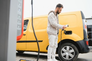 Portrait of a young man standing with charging cable near the charging station