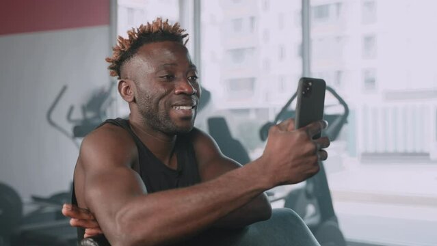young black athletic man is viewing funny video in social networks during rest in gym workout