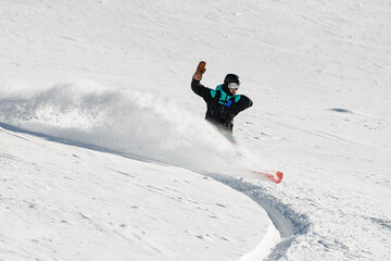 active male snowboarder fast and skilfully descends down a snowy mountain slope