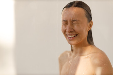 Fototapeta na wymiar Young woman under the trickles of water in pleasure shower. Beautiful girl under the spray of water. Wet happy face