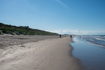 Hot, summer's day with blue skies above Bamburgh beach in Northumberland, UK, with famous castle in distance and tourists on beach