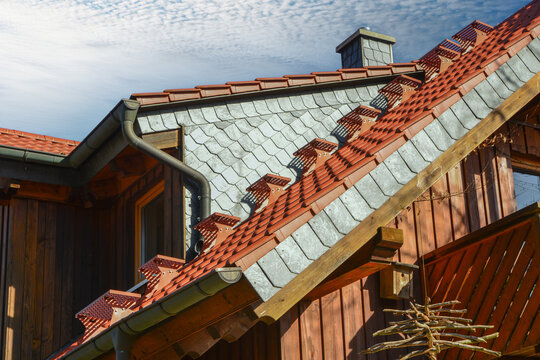 Dachtreppe, Kupfer-Dachrinne und Regenfallrohr, mit Naturschiefer verschindelter Schornstein, verschindelte Gaubenwangen und seitlicher verschindelter Abschluss am Ziegeldach eines Holzst&auml;nderhauses