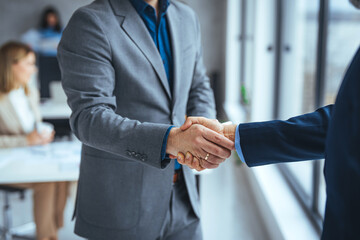 Business people in office suits standing and shaking hands, close-up. Business communication...