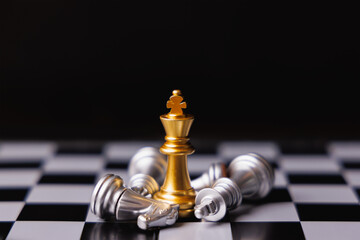 Gold king chess standing in center surround by fallen silver king chess, knight and other pieces in black background. Winner in business competition, marketing strategies and leadership concept. © TimmyTimTim