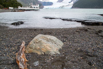 Stone on the shore of the icy lake and in the background view of the glacier and a boat