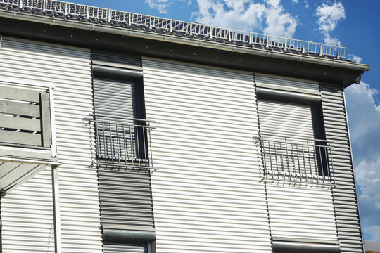 Balkone mit Metall-Geländer und Metall-Plattenverkleidung sowie französische Balkone an moderner Neubau-Hausfront mit Wellblechprofil-Fassadenverkleidung