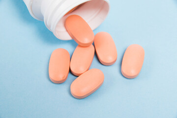 White plastic jar with pink pills of vitamins for women on a blue background