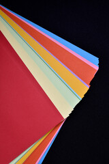 Multicolored sheets of paper on a black background. Colored office paper. A pack of colored paper.