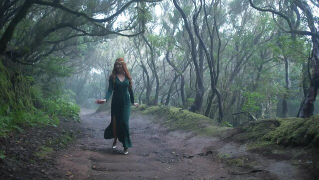 Beautiful woman in an elf costume is walking in a magic green enchanted forest.