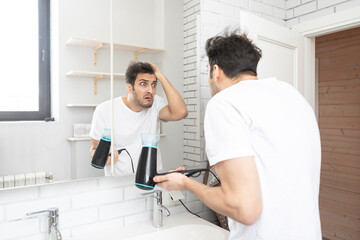 Funny man amusing with hair dryer in the bathroom during daily morning routine. Bad hair day concept - obrazy, fototapety, plakaty