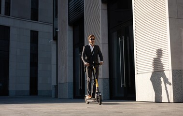 Young business man in a suit riding an electric scooter on a business meeting. Ecological transportation concept.
