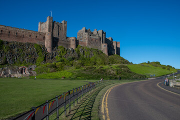 Fototapeta na wymiar View of Bamburgh Castle from the road, against a bright blue summer sky. Northumberland, UK. Platinum Jubilee bunting on nearby fence. Summer 2022