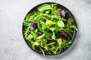 Fototapeta na wymiar Green salad with fresh leaves in black plate. Healthy food, clean eating, diet. Top view.