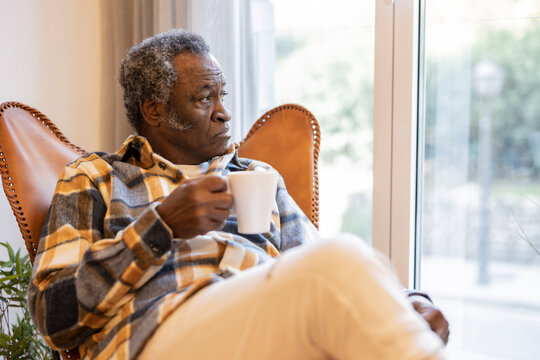 Portrait of a smiling 1960s African American senior man sitting relaxing on the sofa with a cup of coffee. happy pension