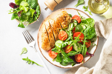 Green salad with roasted chicken steak on white table. Healthy food. Top view with copy space.