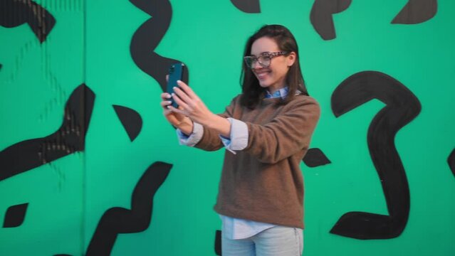 Woman taking a selfie on smartphone camera outside. Adult female person in glasses with leopard print doing selfie photo on mobile phone camera smiling outdoor