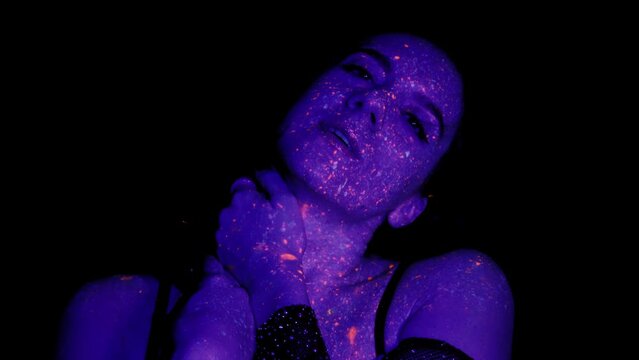 Fashion model woman in neon light, portrait of a beautiful model with fluorescent makeup, body art design in UV, painted face, colorful makeup, on a black background of a girl. Disco dancer in neon
