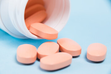 White plastic jar with pink pills of vitamins for women on a blue background