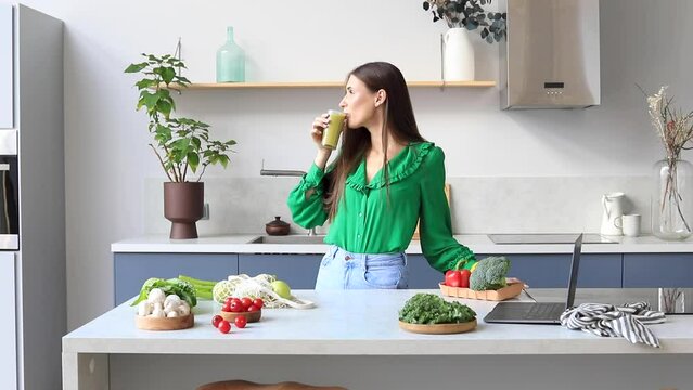 An attractive woman drinks a green smoothie in the kitchen. Healthy eating