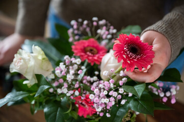 Female florist is putting beautiful spring flowers together in a vase indoors, no visible face