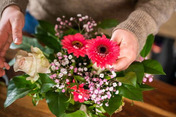 Female florist is putting beautiful spring flowers together in a vase indoors, no visible face