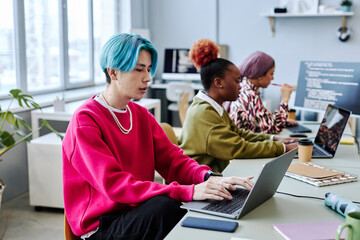Diverse team of gen Z software developers working in office focus on Asian young man with colored...