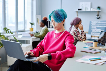 Portrait of Asian young man with colored hair using laptop in modern office, magenta accent