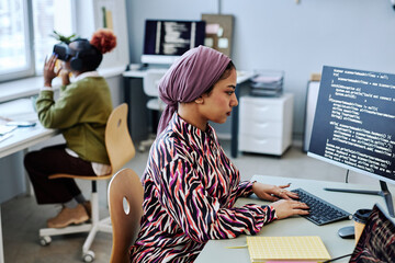 Side view portrait of Muslim young woman as software developer writing code and using computer in...