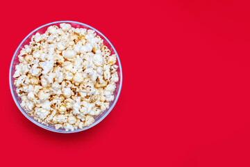 Popcorn in a large glass bowl on a red background from a top view. Crispy classic popcorn snack for watching movies and series. Delicious light snack for watching TV. Free space for text