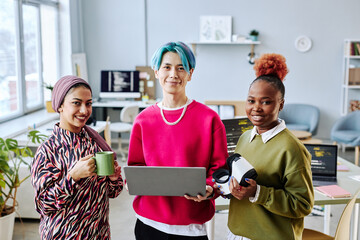 Waist up portrait of multiethnic creative team smiling at camera while standing in office and...