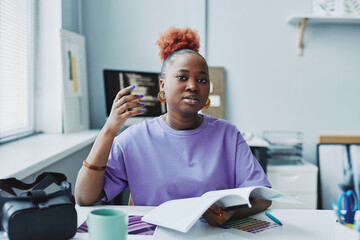 Portrait of black young woman as creative designer wearing purple outfit at workplace and looking at camera