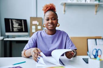 Front view portrait of black young woman wearing purple outfit at workplace and looking at camera