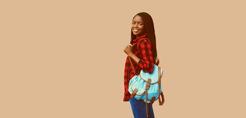 Portrait of young african woman student with backpack on brown background