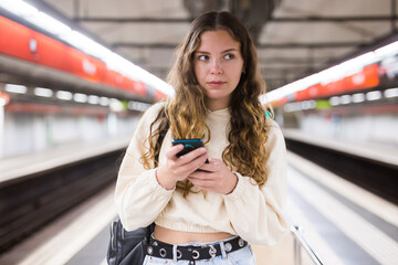 Young european female with mobile waiting the metro on the subway station platform