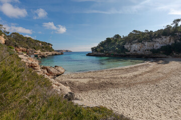 Fototapeta na wymiar Mallorca beach. General view of Cala Llombards beach, with remains of Posidonia Oceanica on the sand. A cove with crystal clear turquoise water, with small houses with jetties for small fishing boats.