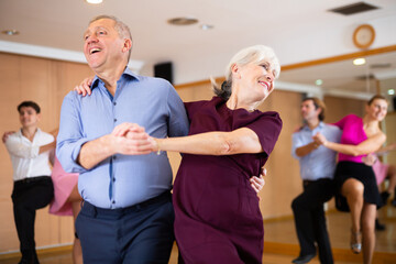 Fototapeta na wymiar Cheerful elderly amateur couple visiting group choreography class, practicing vigorous lindy hop moves. Concept of active lifestyle