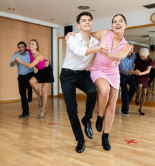 Cheerful young guy and girl practicing ballroom dances in ballroom