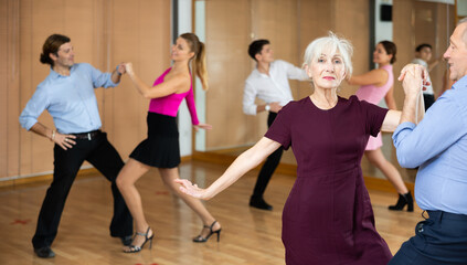 Fototapeta na wymiar elderly couple is engaged in Latin dance studio and learns movements of cha-cha-cha dance