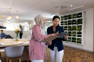 Happy diverse businesswomen with tablets talking in office lounge