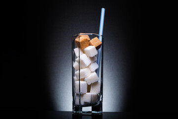 Glass with straw full of sugar and cubes on black background. The concept of prevention of...
