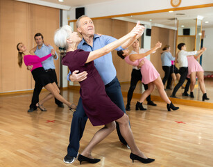 Fototapeta na wymiar Cheerful elderly couple practicing ballroom dances in ballroom