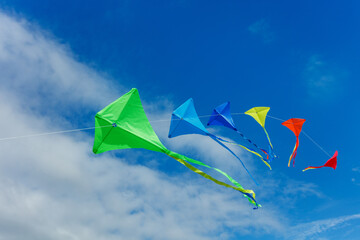 Many beautiful colorful kites fly over blue sky and clouds