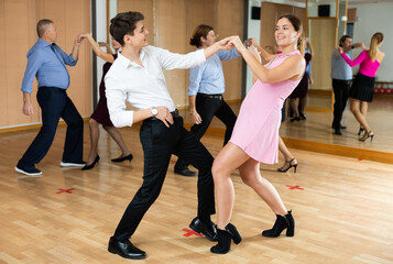 Cheerful young guy and girl practicing ballroom dances in ballroom