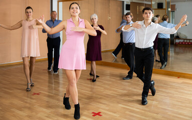 Cheerful young guy and girl practicing ballroom dances in ballroom