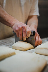 Close up view of baker cutting bread dough with steel scraper in bakery